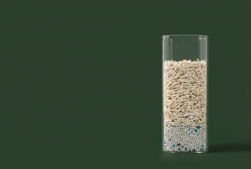 Dust-free tofu cat litter granules in a square glass vessel on a deep green background