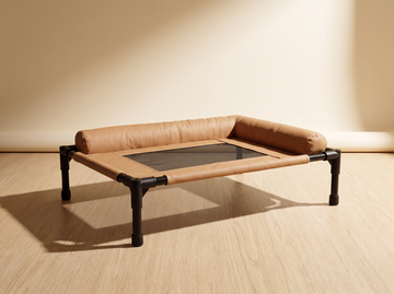 Breeze Cot elevated cat bed in sand vegan leather — studio view on oak floor